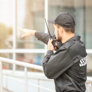 Male security guard using portable radio transmitter near building outdoors